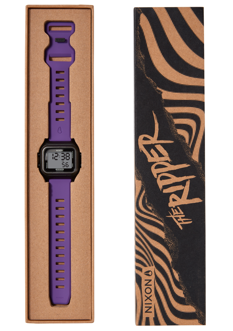 A purple Nixon digital watch with a black face and purple strap is displayed in a brown cardboard box next to a black and brown patterned box sleeve that reads "THE RIPPER".
