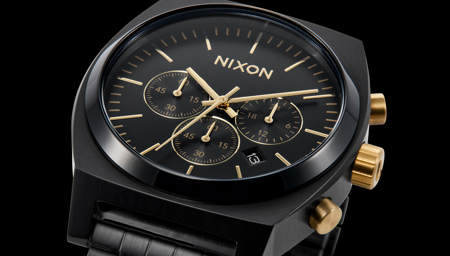 A close-up shot of a black Nixon chronograph watch with gold hands, hour markers, sub-dials, and pushers, set against a dark background.