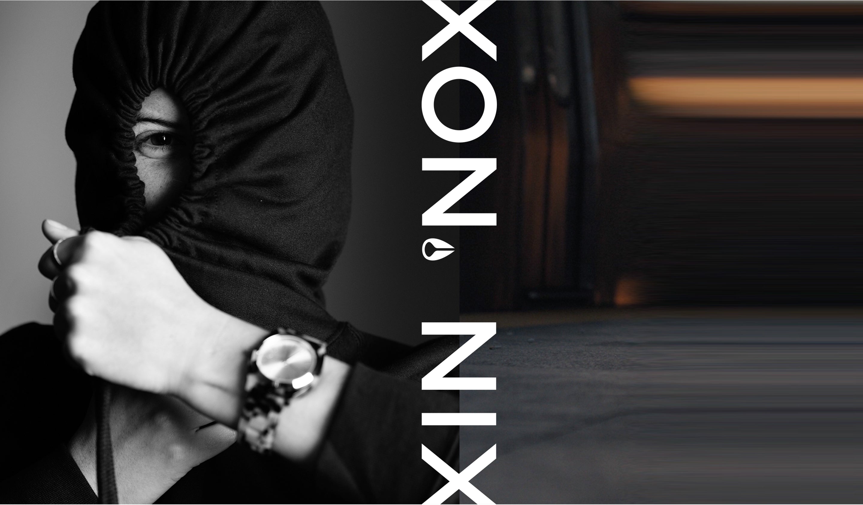 A person in a black hoodie with only one eye visible, wearing a watch on their left wrist, with the text "XON.NIX" vertically on the right side of the image.