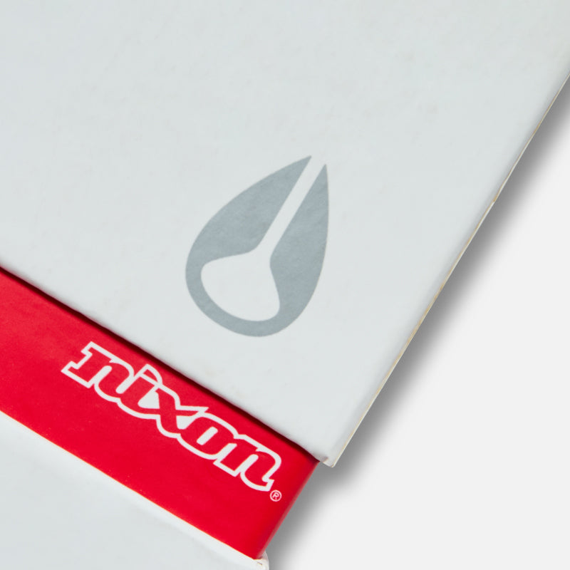 A close-up of a white box with a gray teardrop-shaped logo and a red band with "nixon" in white lettering.