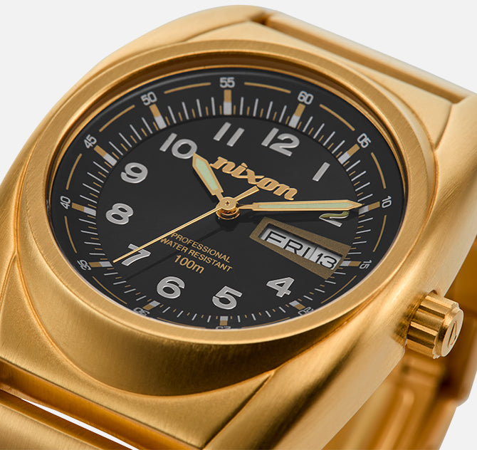 Gold Nixon watch with black face, displaying "FRI 13" and "PROFESSIONAL WATER RESISTANT 100m".